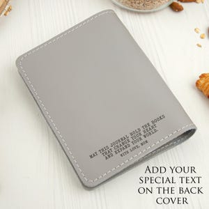 Puede incluir: Un diario gris con costuras blancas alrededor de los bordes. El diario tiene el texto "MAY THIS JOURNAL HOLD THE BOOKS THAT CHANGE YOUR HEART AND EXPAND YOUR WORLD. WITH LOVE, MOM." Texto adicional dice "ADD YOUR SPECIAL TEXT ON THE BACK COVER."
