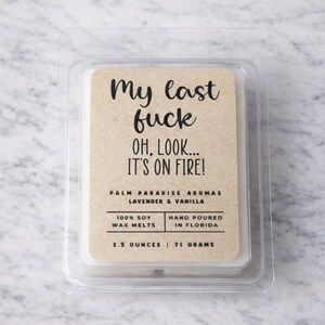 a package of a candle labeled "My last fuck oh, look... IT'S ON FIRE!" The package is placed on a marble surface.