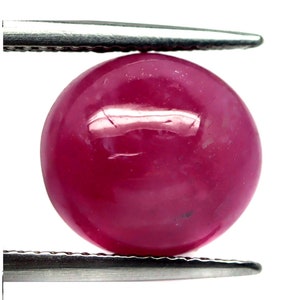 May include: A round, deep red ruby gemstone with a smooth, polished surface.