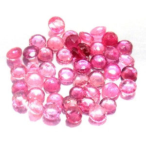 May include: A collection of pink gemstones, likely rubies, in various sizes and shapes. The gemstones are faceted and have a shiny, polished finish.