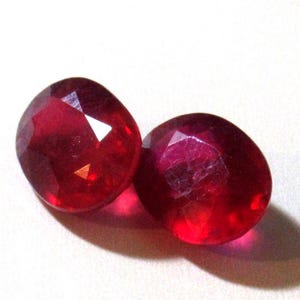 May include: Two bright red gemstone cabochons, each with a faceted surface, are displayed on a white background.