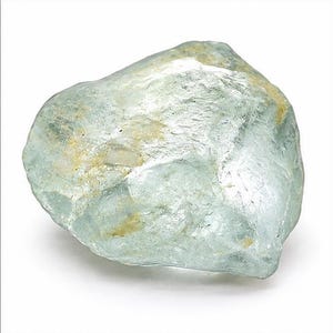May include: A raw, translucent, pale blue-green gemstone with an irregular, multifaceted shape. The surface displays a mix of smooth, glassy areas and rough, textured patches with subtle inclusions of light brown and white mineral deposits.