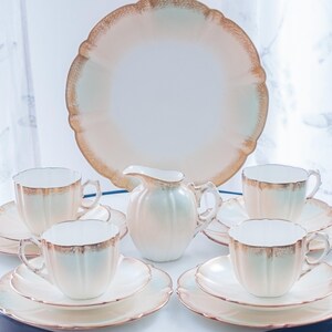 May include: A vintage tea set in a cream and gold colour scheme. The set includes a teapot, creamer, sugar bowl, and four teacups and saucers.