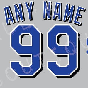 Pu&ograve; includere: Uno sfondo grigio con la scritta "ANY NAME" in blu con un bordo bianco. Sotto, due grandi numeri blu "99" con un bordo bianco e un "99" pi&ugrave; piccolo a destra. Il logo dei Kansas City Royals si trova nell'angolo in basso a sinistra.