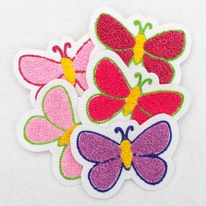 Pode incluir: Quatro patches de borboleta de feltro bordados em rosa, roxo e vermelho com centros amarelos. As borboletas estão dispostas em um cacho.
