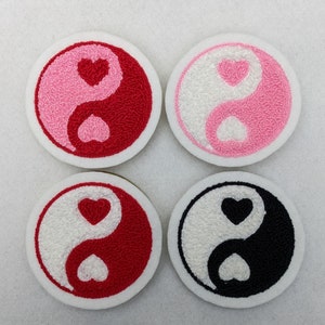 Könnte beinhalten: Vier gestickte Aufnäher mit einem Yin-Yang-Symbol mit Herzen in der Mitte. Die Aufnäher sind weiß, rosa, rot und schwarz.