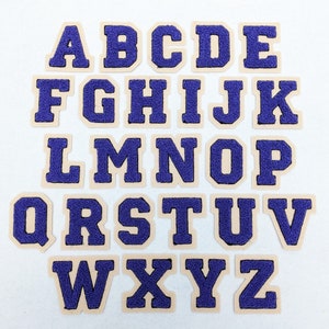 May include: A set of 26 felt letter patches in a purple colour with a white outline. The letters are in uppercase and are arranged in alphabetical order.