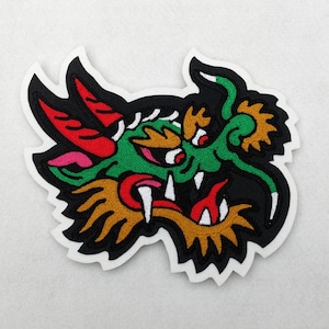 May include: Green, red, and white embroidered dragon head patch with a black background. The dragon has a fierce expression with sharp teeth and a long, curled horn.
