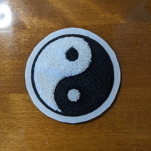 May include: A white and black yin yang symbol embroidered on a round, white felt patch.