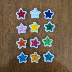 May include: Twelve star-shaped embroidery hoops with different colored embroidery floss inside. The hoops are arranged in three rows of four.