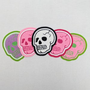May include: Five embroidered skull patches in different colors. The skulls are pink, green, white, and black. The patches are perfect for adding a spooky touch to clothing, bags, or other accessories.