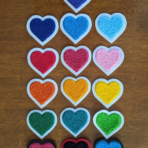 May include: A set of 15 felt heart patches in various colors, including blue, pink, red, orange, yellow, green, and black. The hearts are arranged in a pyramid shape on a wooden surface.