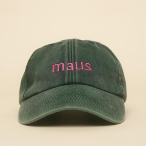 Könnte beinhalten: Dunkelgrüne Baseballkappe mit dem Wort "maus" in Rosa gestickt. Die Kappe hat einen gebogenen Schirm und ein klassisches, unstrukturiertes Design. Der Hut ist aus einem weichen, abgenutzten Material.