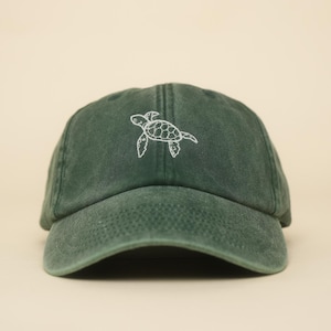 Pode incluir: Boné de beisebol verde escuro com um design de tartaruga marinha bordada em branco. O boné tem uma aba curva e um design clássico de seis painéis, adequado para uso diário.