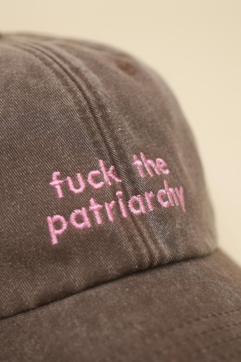 K&ouml;nnte beinhalten: Braune Baseballkappe mit dem in rosa gestickten Schriftzug "fuck the patriarchy". Die Kappe besteht aus einem strukturierten Stoff und hat einen gebogenen Schirm. Der Text ist mittig auf der Vorderseite.