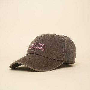 K&ouml;nnte beinhalten: Dunkelgraue Baseballkappe mit gebogenem Schirm. Auf der Kappe ist der Text "Fuck the patriarchy" in Pink gestickt. Der Hut ist aus weichem, abgenutztem Material.