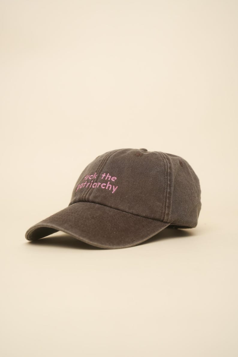 K&ouml;nnte beinhalten: Dunkelgraue Baseballkappe mit gebogenem Schirm. Auf der Kappe ist der Text "Fuck the patriarchy" in Pink gestickt. Der Hut ist aus weichem, abgenutztem Material.