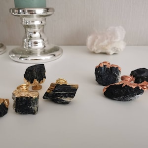 Può includere: Una collezione di pomelli in tormalina nera con dettagli in foglia d'oro e rame. I pomelli, di varie forme, sono perfetti per aggiungere un tocco naturale e unico ai mobili. Sono esposti su una superficie bianca.