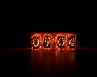 May include: A close-up of a vintage-style digital clock displaying the time 09:04. The clock has four orange-red glowing Nixie tubes, each displaying a single digit. The clock is set against a dark background.