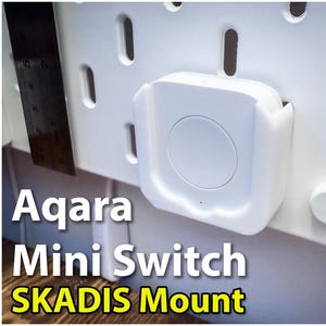 May include: A white Aqara Mini Switch mounted on a white SKADIS wall panel. The switch has a round button and is attached to the panel with a white plastic mount.