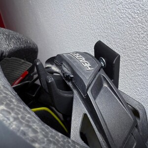 Puede incluir: Un soporte de casco negro con la palabra "HEADER" impresa en &eacute;l. El soporte est&aacute; montado en una pared blanca.