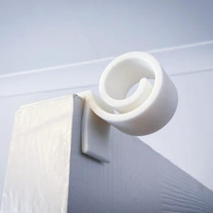 May include: White plastic decorative scroll design for a door or window trim. The scroll is attached to a white surface.