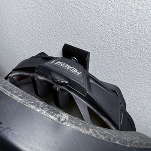 Puede incluir: Un casco de bicicleta negro con la palabra "HEADSET" impresa en el lateral, colgado de un soporte de pared negro.