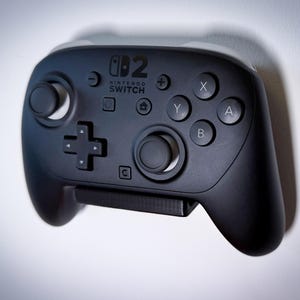 May include: A black Nintendo Switch Pro Controller with white accents. The controller features a directional pad, analog sticks, and action buttons labeled X, Y, A, and B. The Nintendo Switch logo is visible.