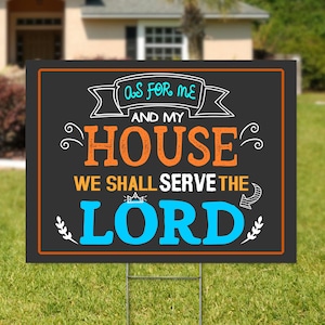 May include: Black yard sign with white and orange text that reads "As for me and my house we shall serve the Lord". The text is in a decorative font with a crown above the word "Lord".
