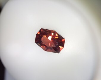 May include: A red-brown gemstone with a faceted octagonal shape.
