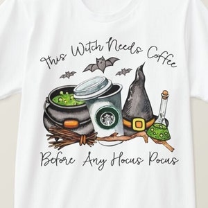Pode incluir: Camiseta branca com um gráfico de um chapéu de bruxa, um caldeirão, uma xícara de café e morcegos. O texto diz "This Witch Needs Coffee Before Any Hocus Pocus".
