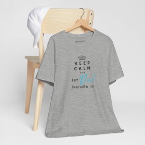 Könnte beinhalten: Graues T-Shirt mit dem Text "Keep Calm and let Dad handle it" in schwarzer und blauer Schrift. Eine Krone befindet sich über dem Text "Keep Calm".