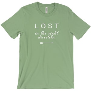 May include: A sage green t-shirt with the words "LOST in the right direction" in white script and a white arrow graphic. The shirt is made of a soft material and has a classic crew neck.
