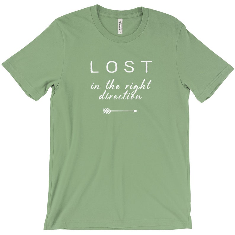 May include: A sage green t-shirt with the words "LOST in the right direction" in white script and a white arrow graphic. The shirt is made of a soft material and has a classic crew neck.