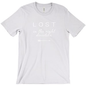 May include: A light gray t-shirt with the words "LOST in the right direction" printed in white. An arrow graphic is below the text. The shirt has a crew neck and short sleeves.