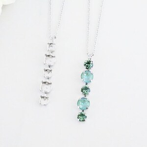 May include: Two silver necklaces with a chain link design. One necklace has a pendant with five green crystal stones.