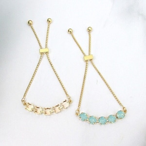 May include: Two gold adjustable bracelets with a row of small, round, clear stones. One bracelet has light blue stones and the other has light peach stones.