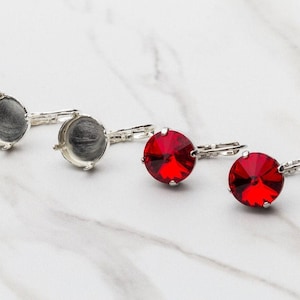 May include: Two pairs of silver earrings with a round setting. One pair has clear settings and the other pair has red gemstones.