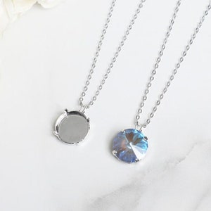 May include: Two silver necklaces with round pendants. One pendant is empty and the other has a blue crystal.