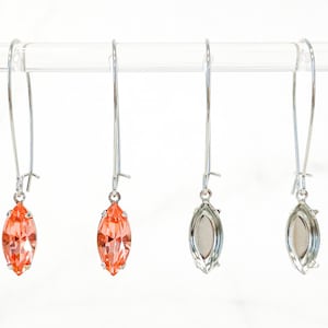 May include: A pair of silver dangle earrings with a peach-colored marquise-shaped stone. The earrings are hanging from a clear rod.