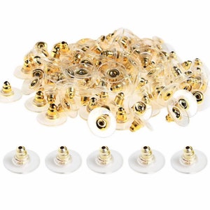 May include: A large pile of gold-toned earring backs with clear plastic backing. There are six individual earring backs in the bottom row of the image.