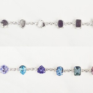 May include: Two silver bracelets with different colored gemstones. The top bracelet has clear, gray, and black gemstones. The bottom bracelet has blue, purple, and green gemstones.