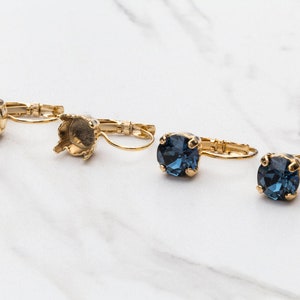 May include: A pair of gold-tone earring settings with a blue crystal stone. The settings are open and ready to be filled with a crystal.