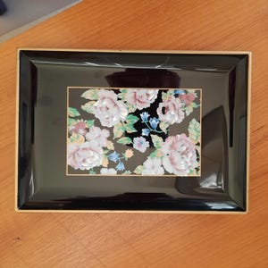 May include: A black lacquered tray with a gold trim and a floral design featuring pink, white, and blue flowers on a black background.