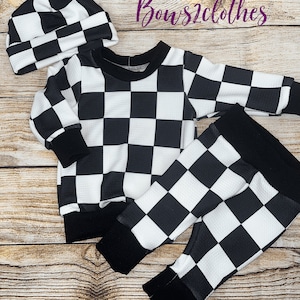 May include: Black and white checkered baby outfit with a long-sleeved shirt and pants. The outfit also includes a black and white checkered beanie.