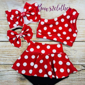 May include: A red and white polka dot baby outfit set. The set includes a headband with a large bow, a smaller bow, a one-shoulder top, and a skirt with a black bottom. The text "Bows2clothes" is visible in the image.