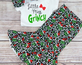 May include: A white onesie with the text "Little Miss Grinch" in green and red. A green and black leopard print headband with a red bow. A green and black leopard print skirt with a green Grinch face and red Santa hat pattern.