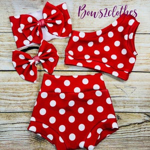 May include: Red and white polka dot swimsuit with a matching headband. The swimsuit has a one-shoulder top and high-waisted bottoms. The headband is a large bow.