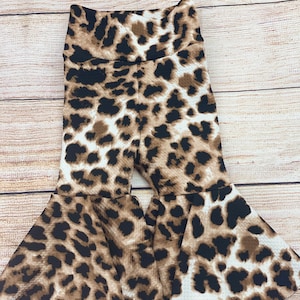 May include: Brown, black, and white leopard print bell bottom pants for a child. The pants have a wide leg opening and a high waist.