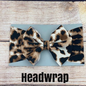 May include: A brown and black leopard print headband with a large bow. The headband is on a light gray background with the word "Headwrap" printed below it.